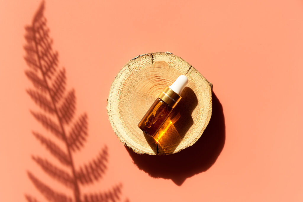 Amber Glass Dropper Bottle On A Woodcut In The Sunlight With Eucalyptus Flower Shadows. Top View